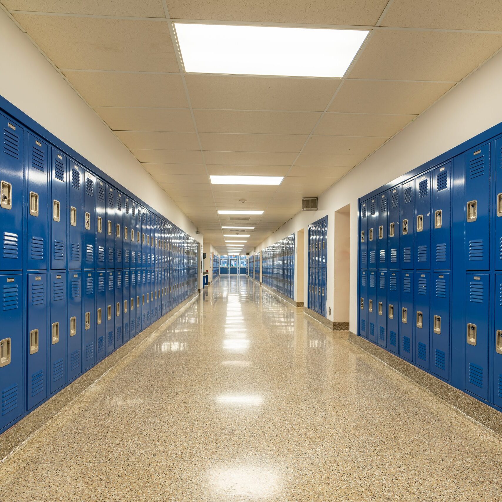 Typical, nondescript USA empty school hallway with royal blue metal lockers along both sides of the hallway.